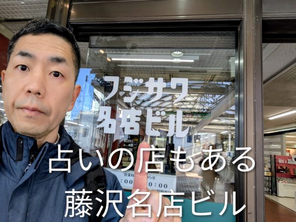 藤沢名店ビルの自動ドアのビル名を指さす占い師の手相の後藤