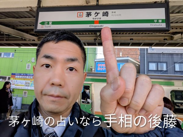 茅ヶ崎駅で占い師の手相の後藤が茅ヶ崎の駅の看板を指さしている